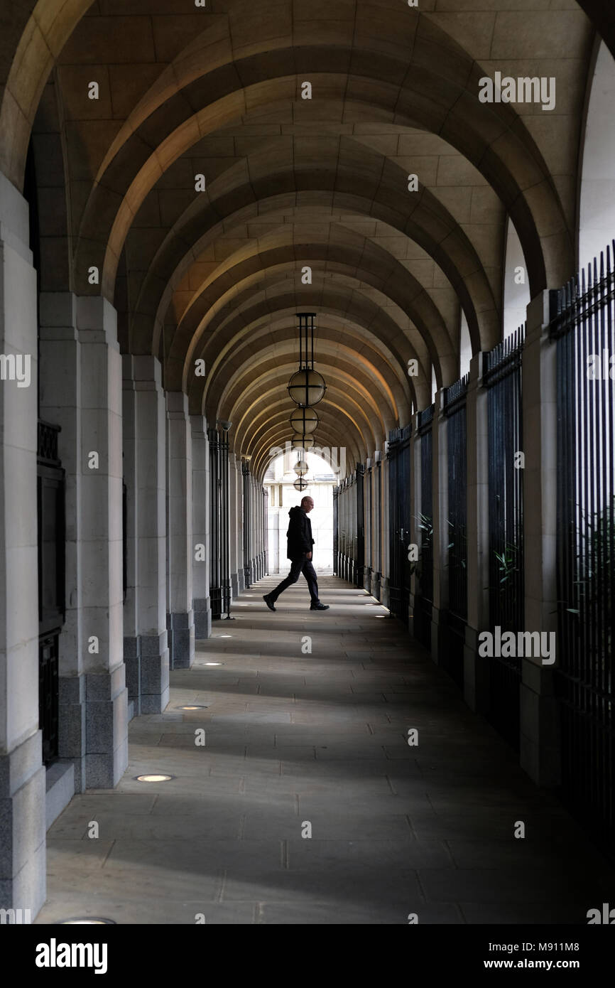 Un uomo camminare sotto le arcate al Savoy Place, Londra. Foto Stock