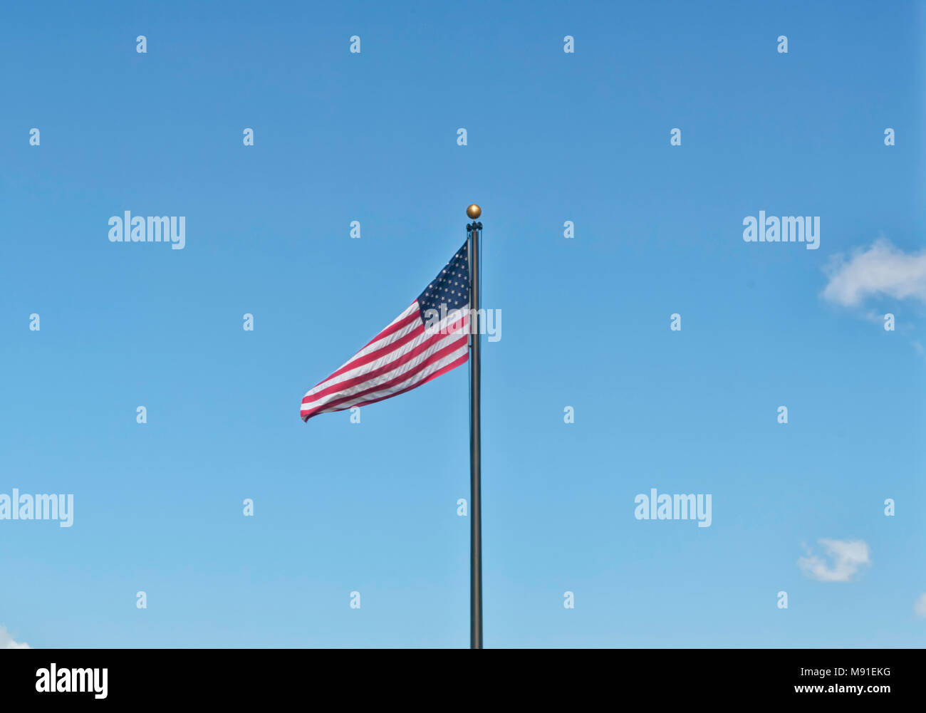 Una bandiera americana su un black metal pole tessitura nel cielo chiaro il 4 di luglio. A stelle e strisce su uno sfondo ideale per copyspace. Foto Stock