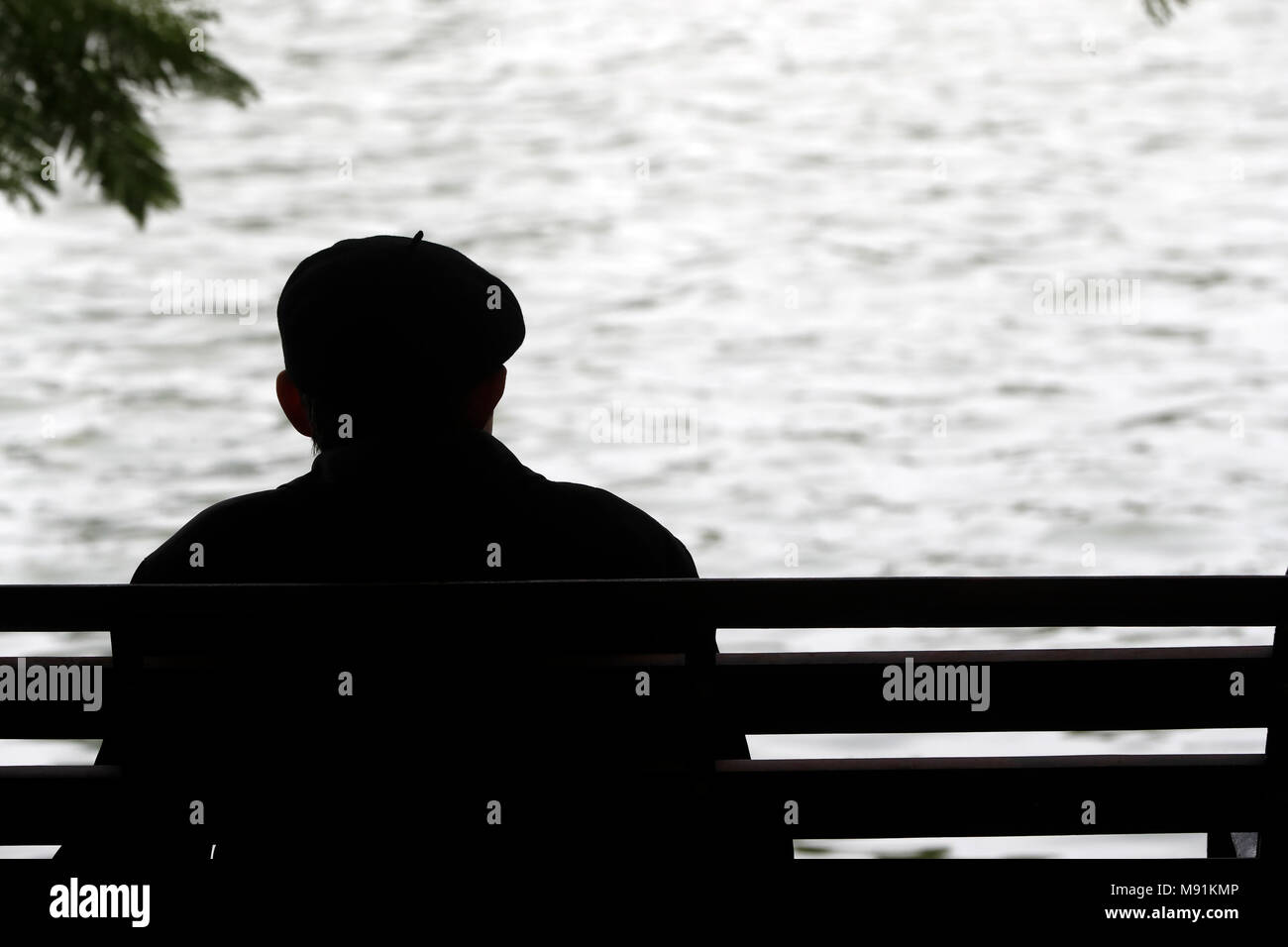 Uomo seduto su una panchina di fronte lago Hoan Kiem. Hanoi. Il Vietnam. Foto Stock