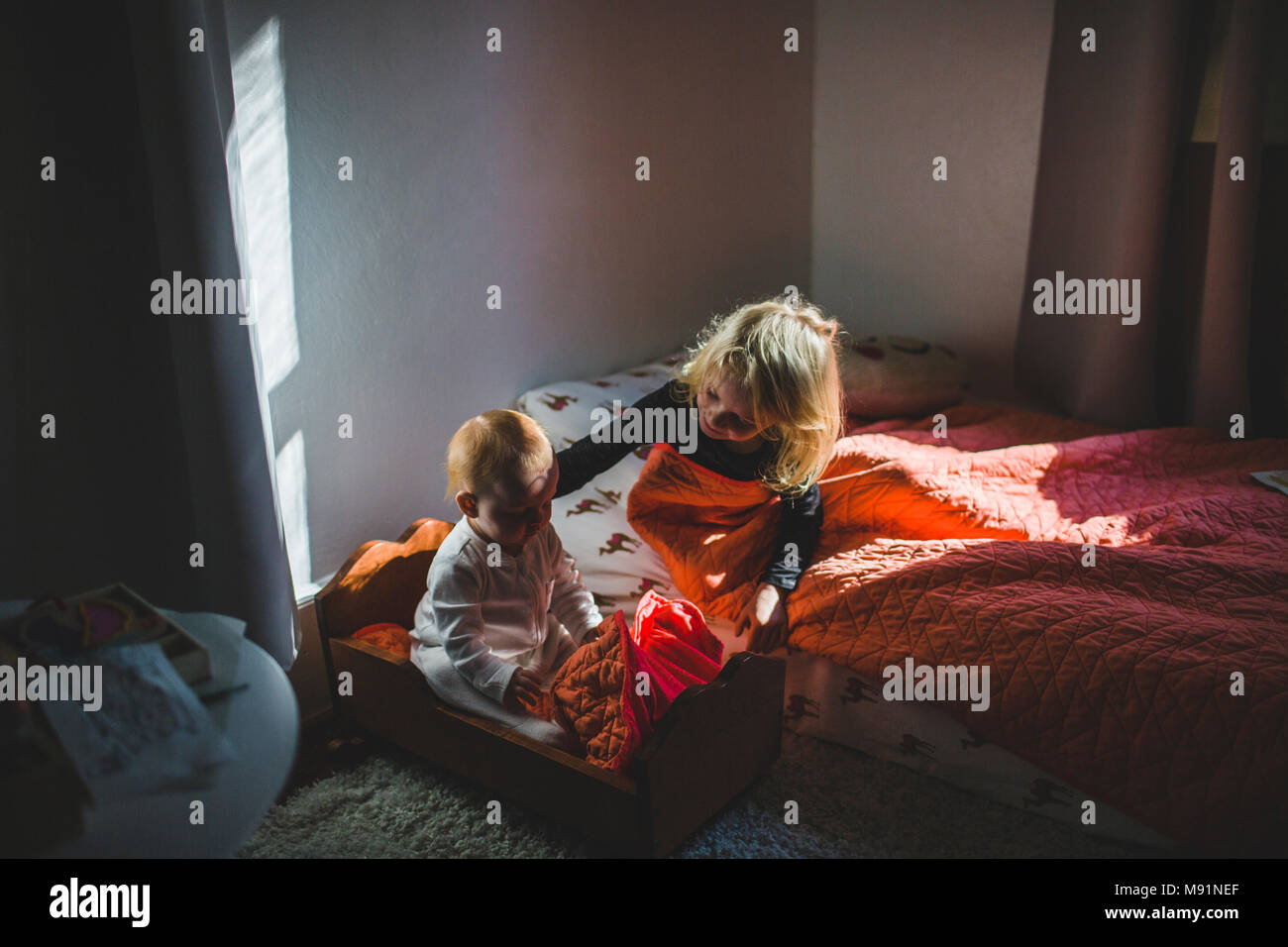 Ragazza che conforta il bambino nella culla babydoll trendy camera per bambini luce drammatica Foto Stock