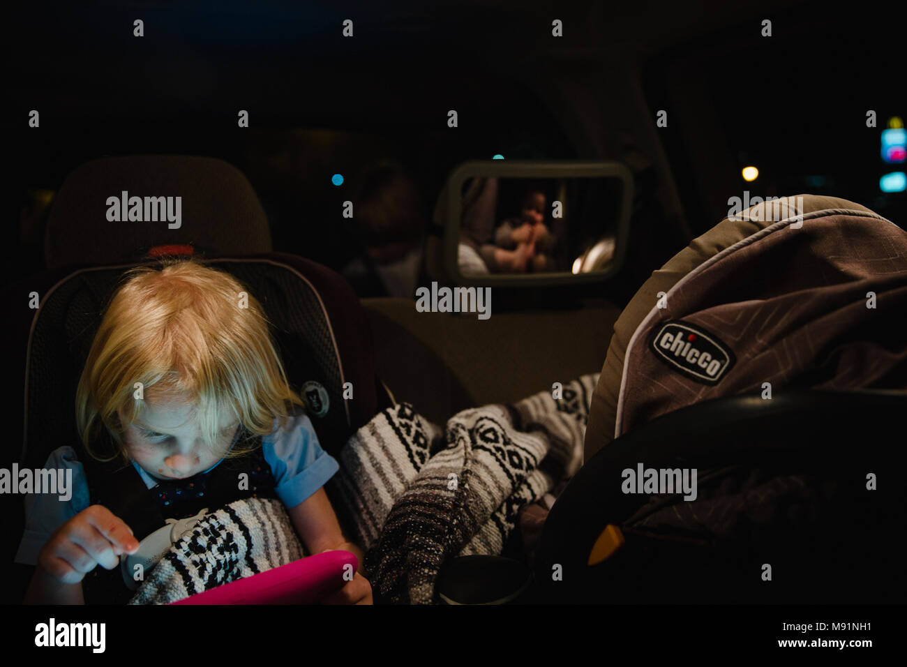 Bambina gioca sul tablet ipad in backseat mentre il bambino dorme in carseat tempo di notte Foto Stock
