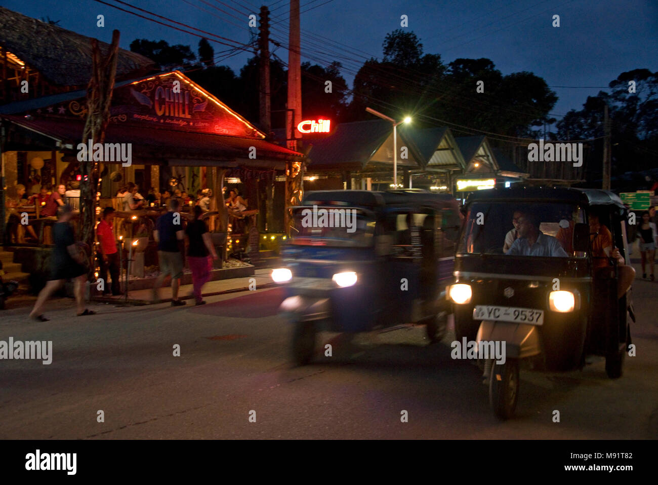 La strada principale di Ella sera notte tempo con tuk tuks, ristoranti, bar, turisti e gente del posto. Rallentare la velocità dello shutter e high iso in modo motion blur. Foto Stock