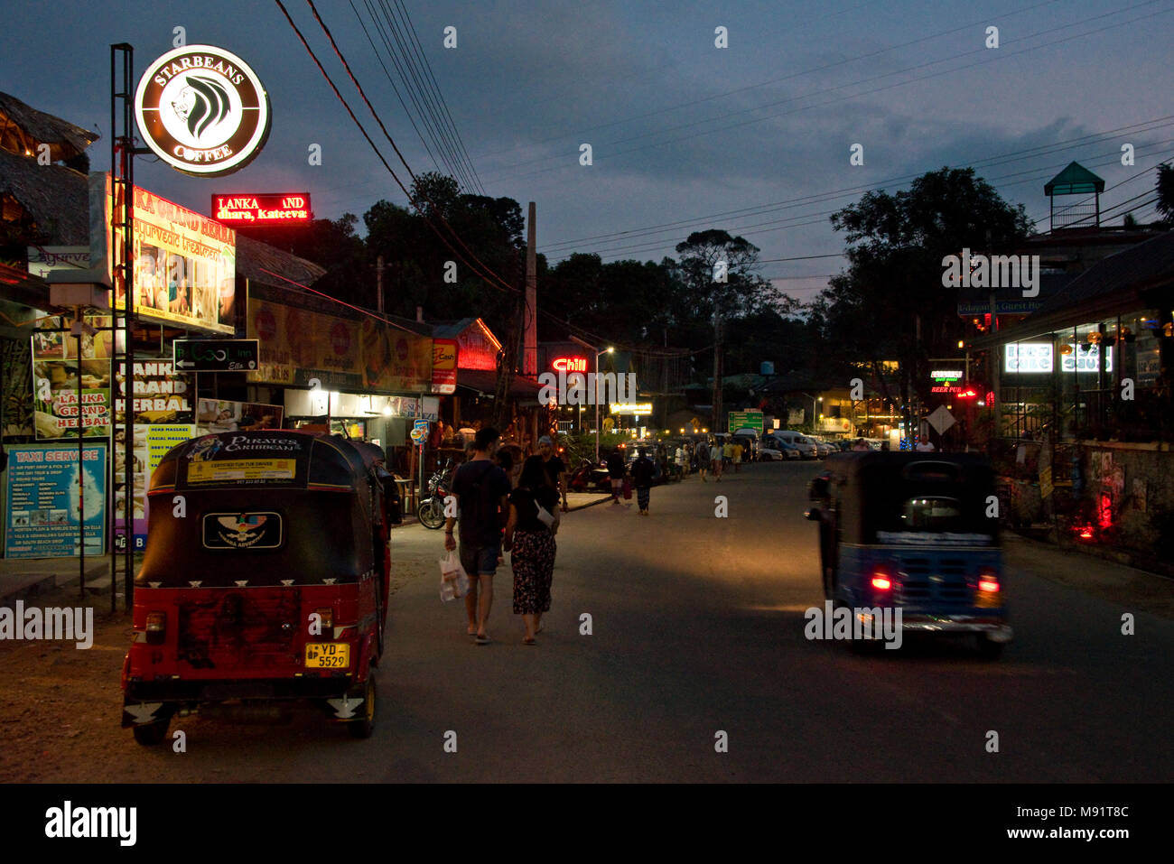 La strada principale di Ella sera notte tempo con tuk tuks, ristoranti, bar, turisti e gente del posto. Rallentare la velocità dello shutter e high iso in modo motion blur. Foto Stock