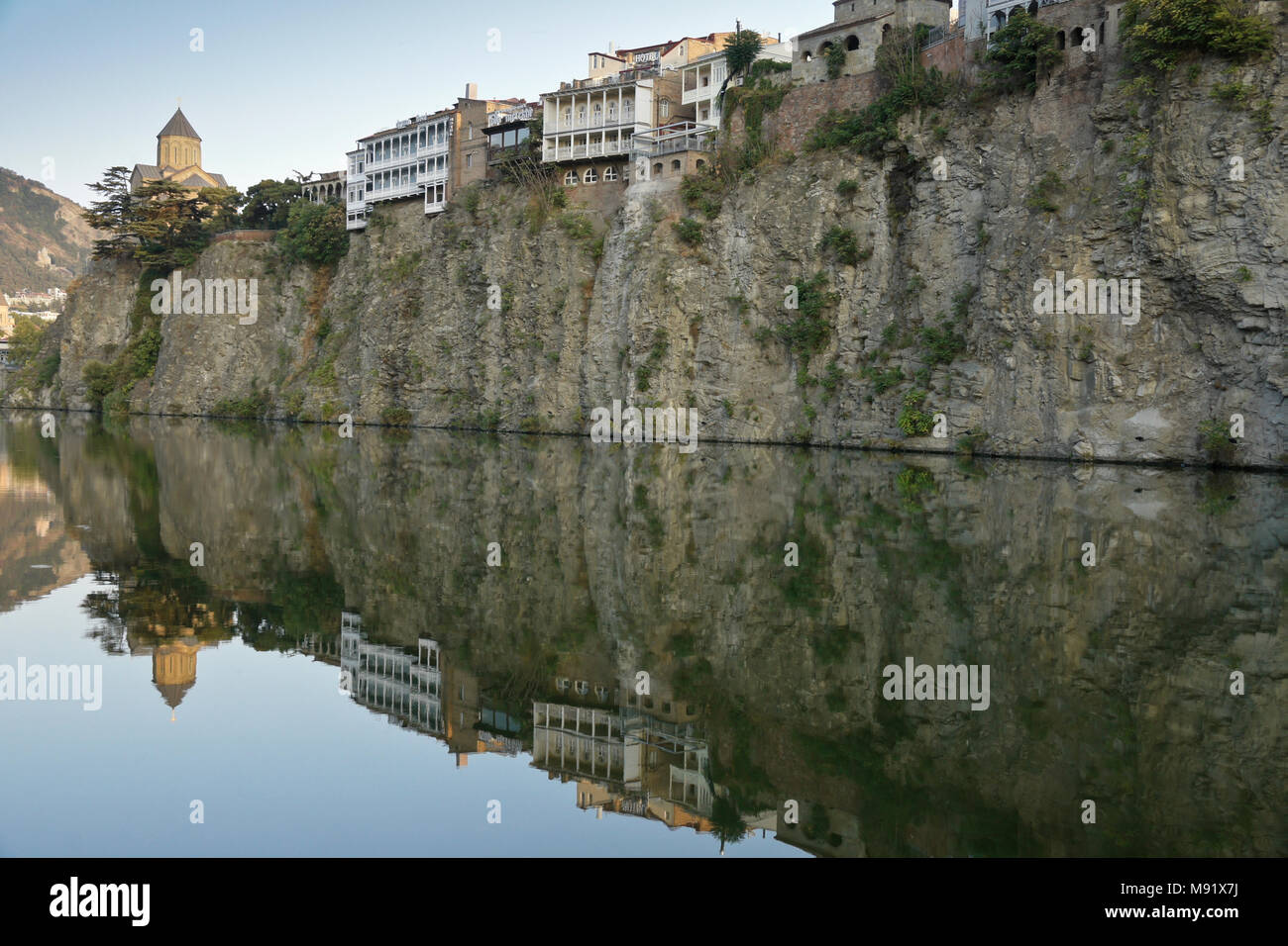 Chiesa di Metekhi e balconied edifici su di una scogliera rocciosa si riflettono nelle acque tranquille del Mtkvari Kura (Fiume), Tbilisi, Georgia Foto Stock