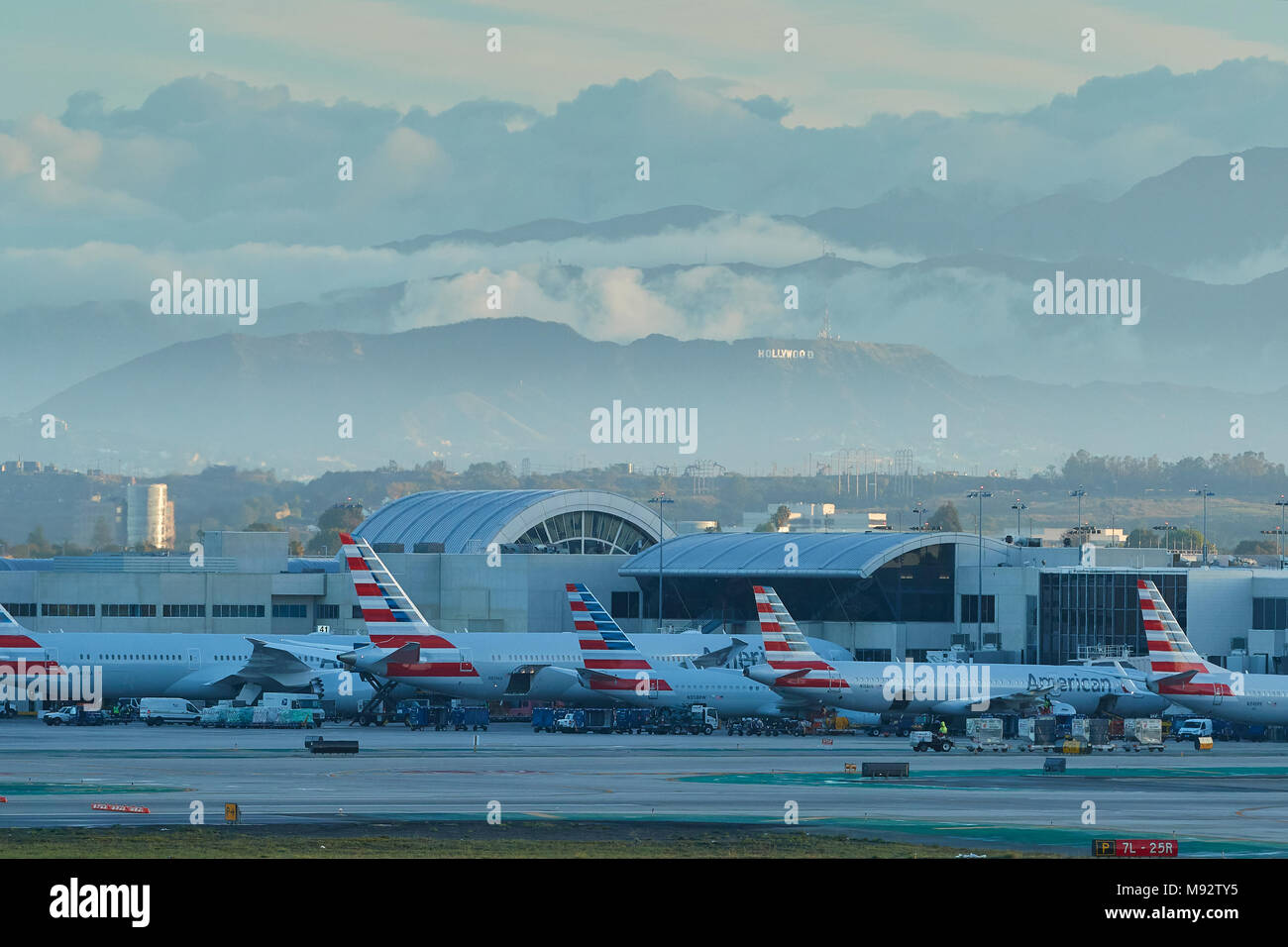 La mattina presto presso l'Aeroporto Internazionale di Los Angeles LAX. Parcheggiato American Airlines piani. Il segno di Hollywood, dietro, illuminata dal sole nascente. Foto Stock