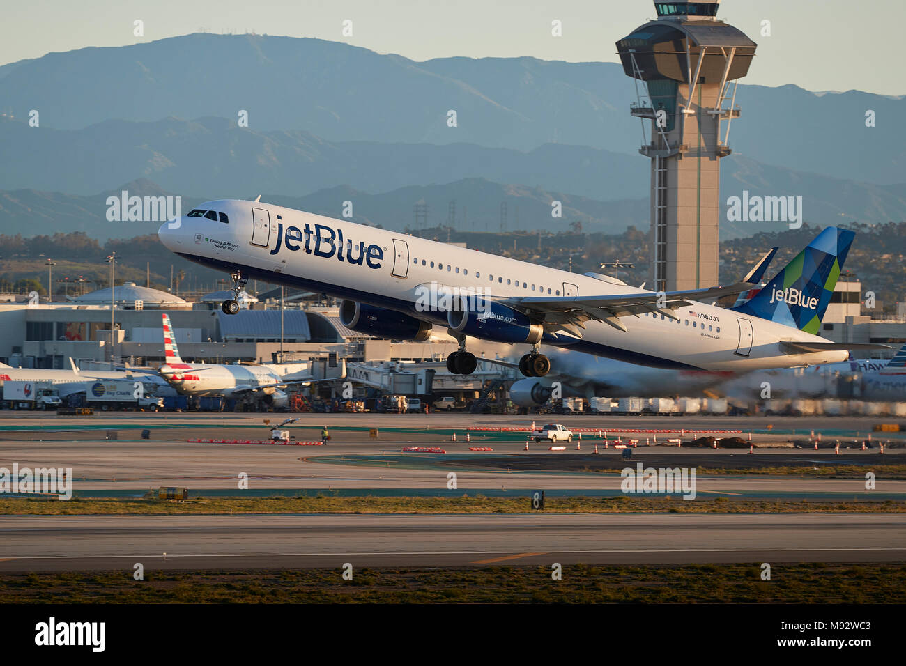 JetBlue Airways Airbus A321 aereo Jet decollo dall'Aeroporto Internazionale di Los Angeles LAX, nelle prime ore del mattino, la nuova torre di controllo dietro. Foto Stock