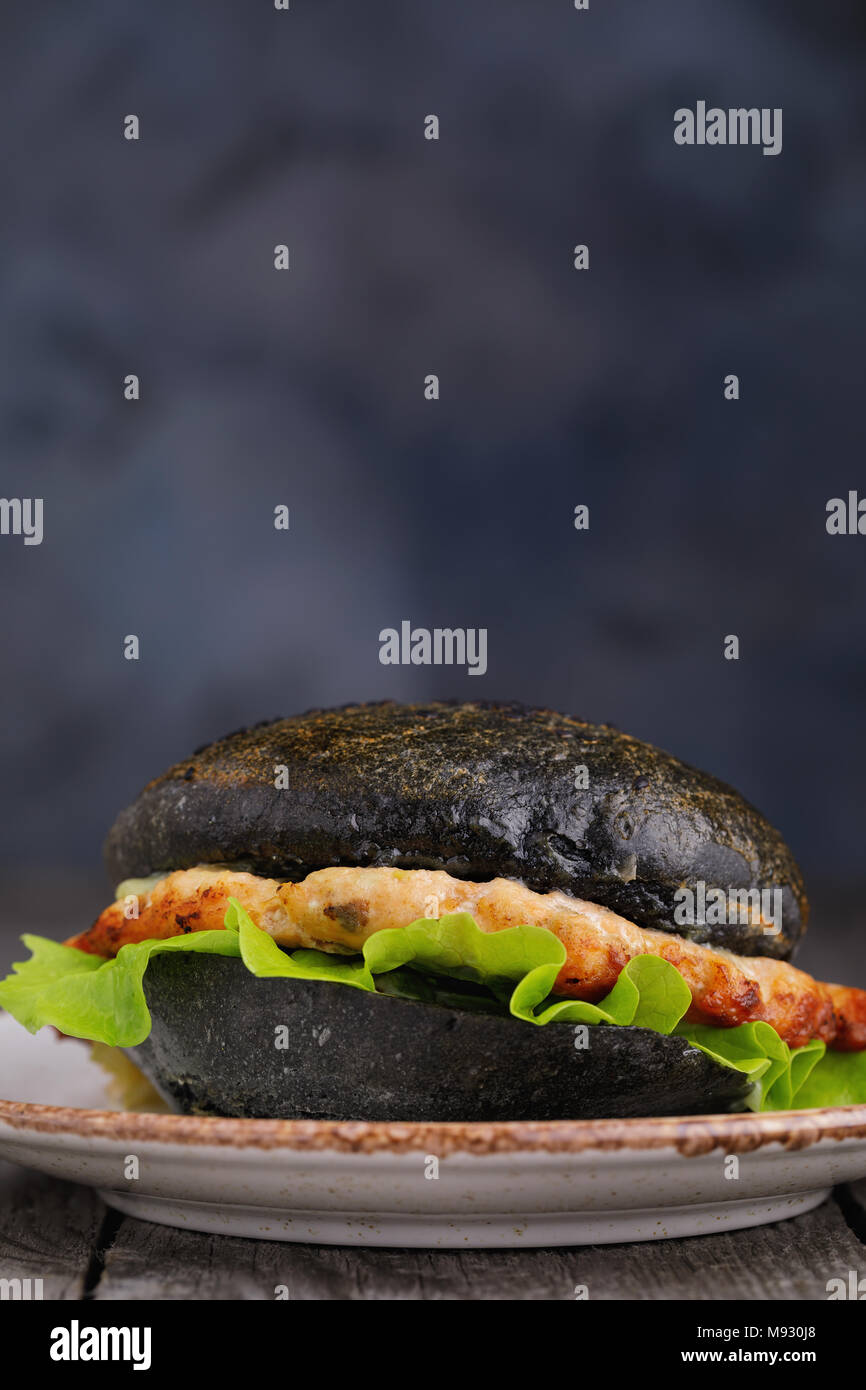 Cucinata fresca hamburger con rotolo di colore nero, verdure e salmone cotoletta. Sandwich fatti in casa closeup con spazio per il testo Foto Stock