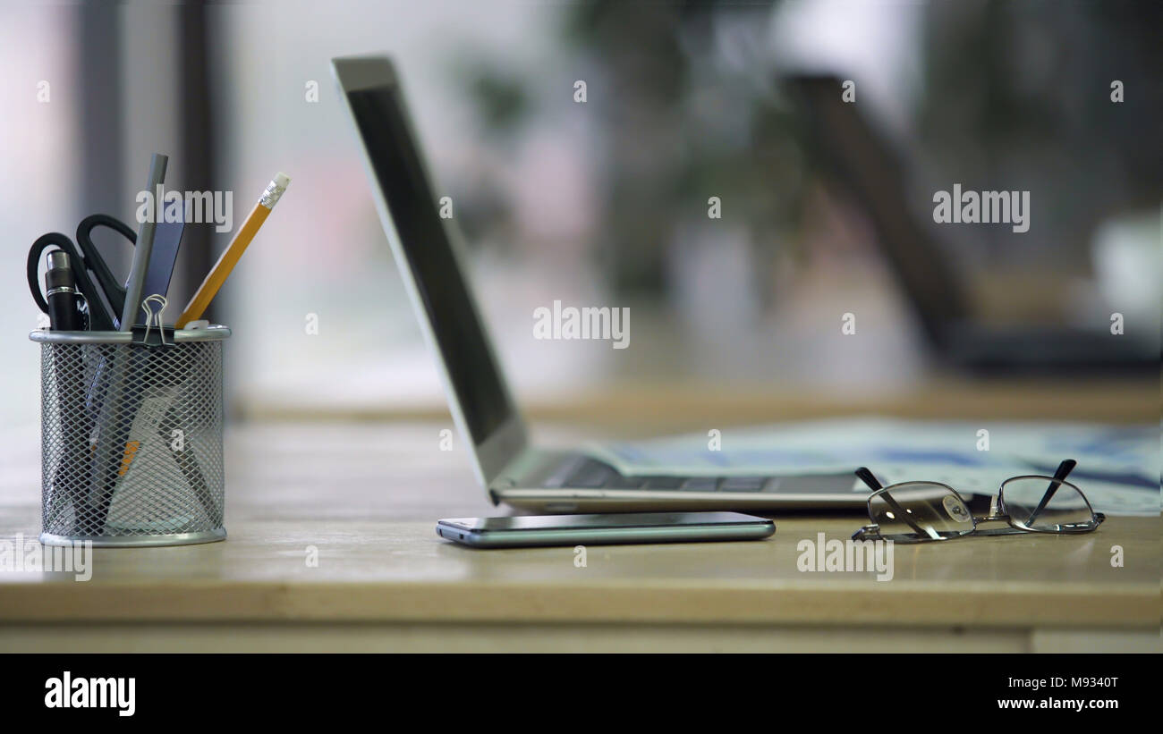 Vista dettagliata del posto di lavoro presso la società office, portapenne, occhiali, laptop sulla scrivania Foto Stock