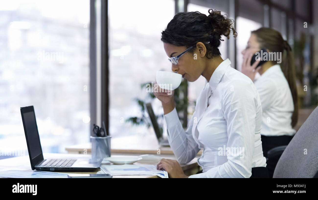 Femmina attraente lavoratore di ufficio a bere caffè e la lettura dei grafici Foto Stock