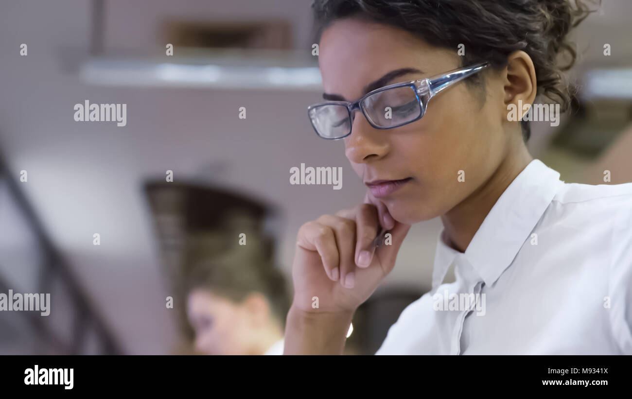 Razza mista femmina in occhiali pensando a progetto presso ufficio, nuove idee Foto Stock