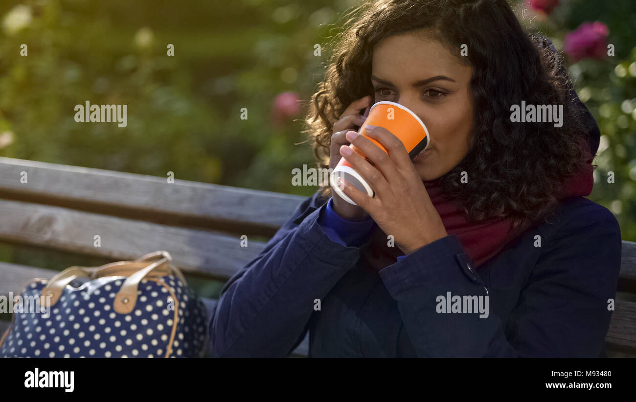 Donna attraente parlando sullo smartphone, bere il caffè caldo all'esterno, fredda giornata Foto Stock