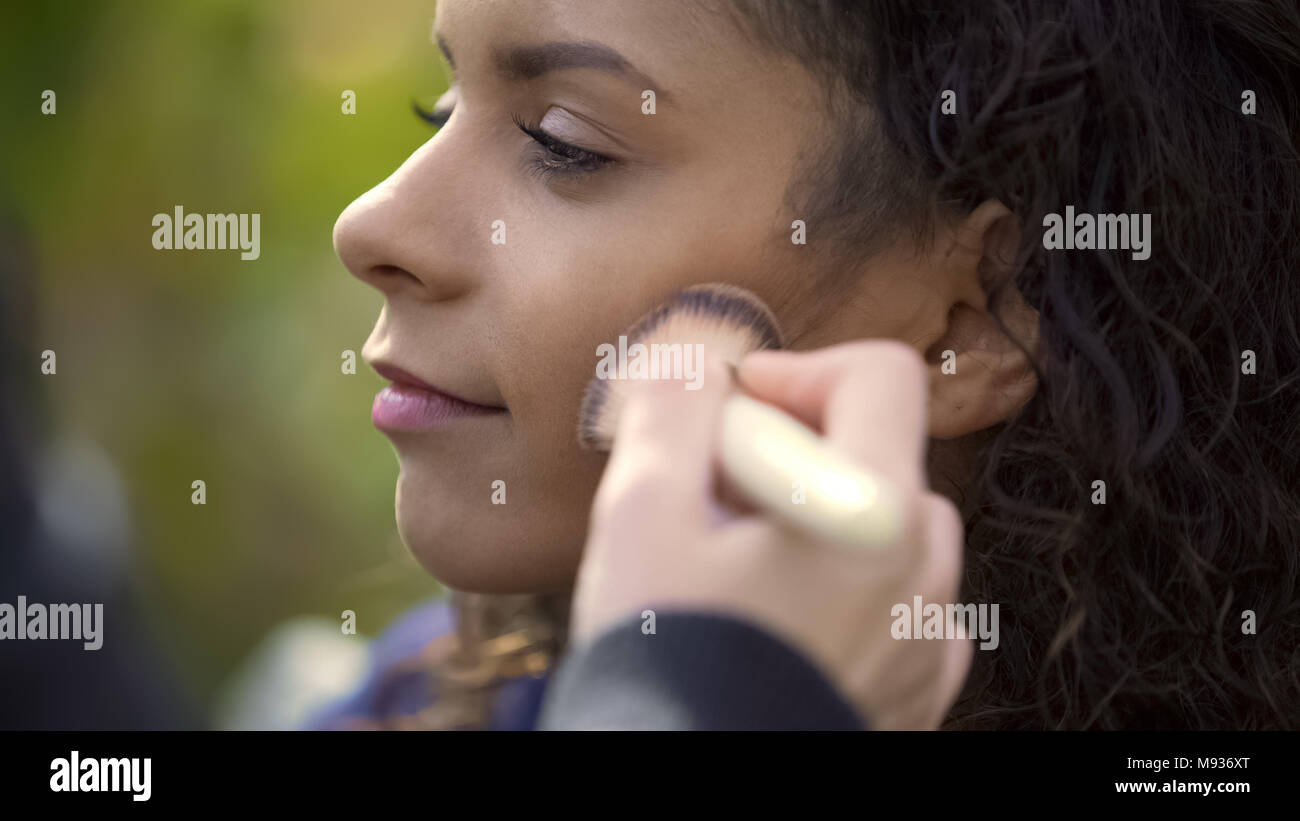 Trucco artisti applicando la polvere con una spazzola sulle guance di pretty razza mista modello Foto Stock