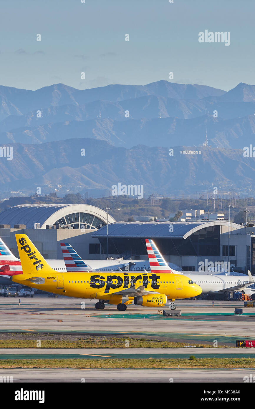 Spirito le compagnie aeree A319, in brillante livrea gialla in rullaggio per il terminale passeggeri all'Aeroporto Internazionale di Los Angeles LAX, il segno di Hollywood dietro. Foto Stock