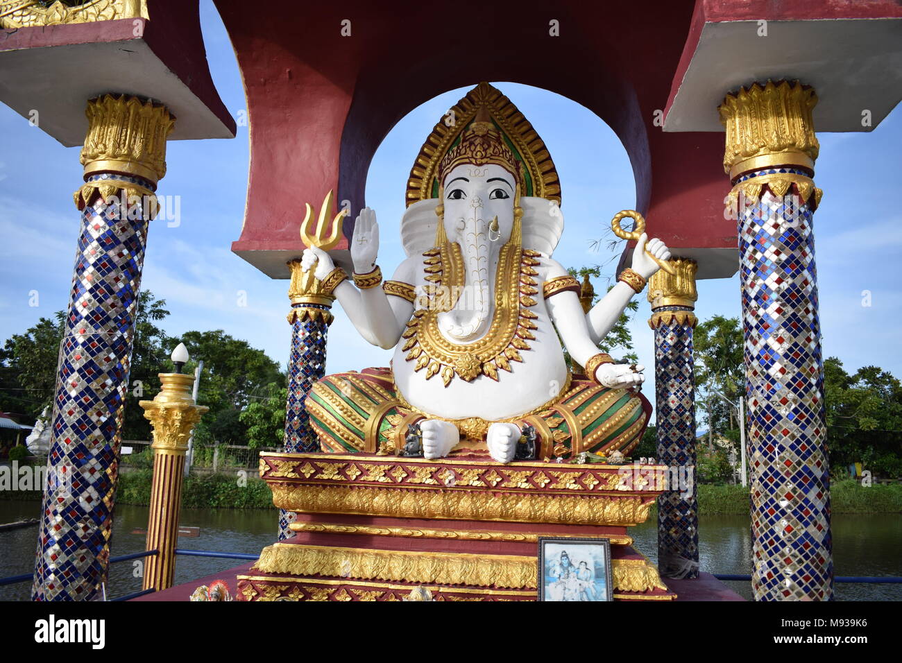 Ganesha elephant face statua in un Wat Plai Laem tempio buddista sotto un tetto poco supportato da 4 blu scolpito pilastri su un lago surrou sfondo Foto Stock