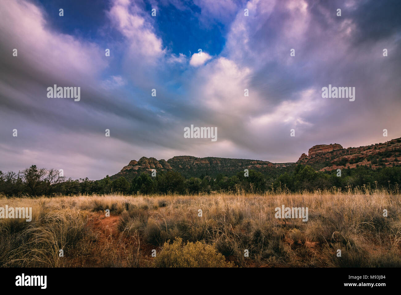 Drammatica nuvole nel cielo sopra una montagna al tramonto lungo la verde valle School Road, Sedona, in Arizona Foto Stock