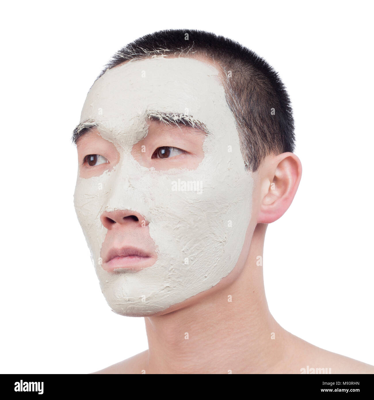 Carino il ragazzo asiatico con argilla maschera facciale guardando dal lato isolato su bianco Foto Stock