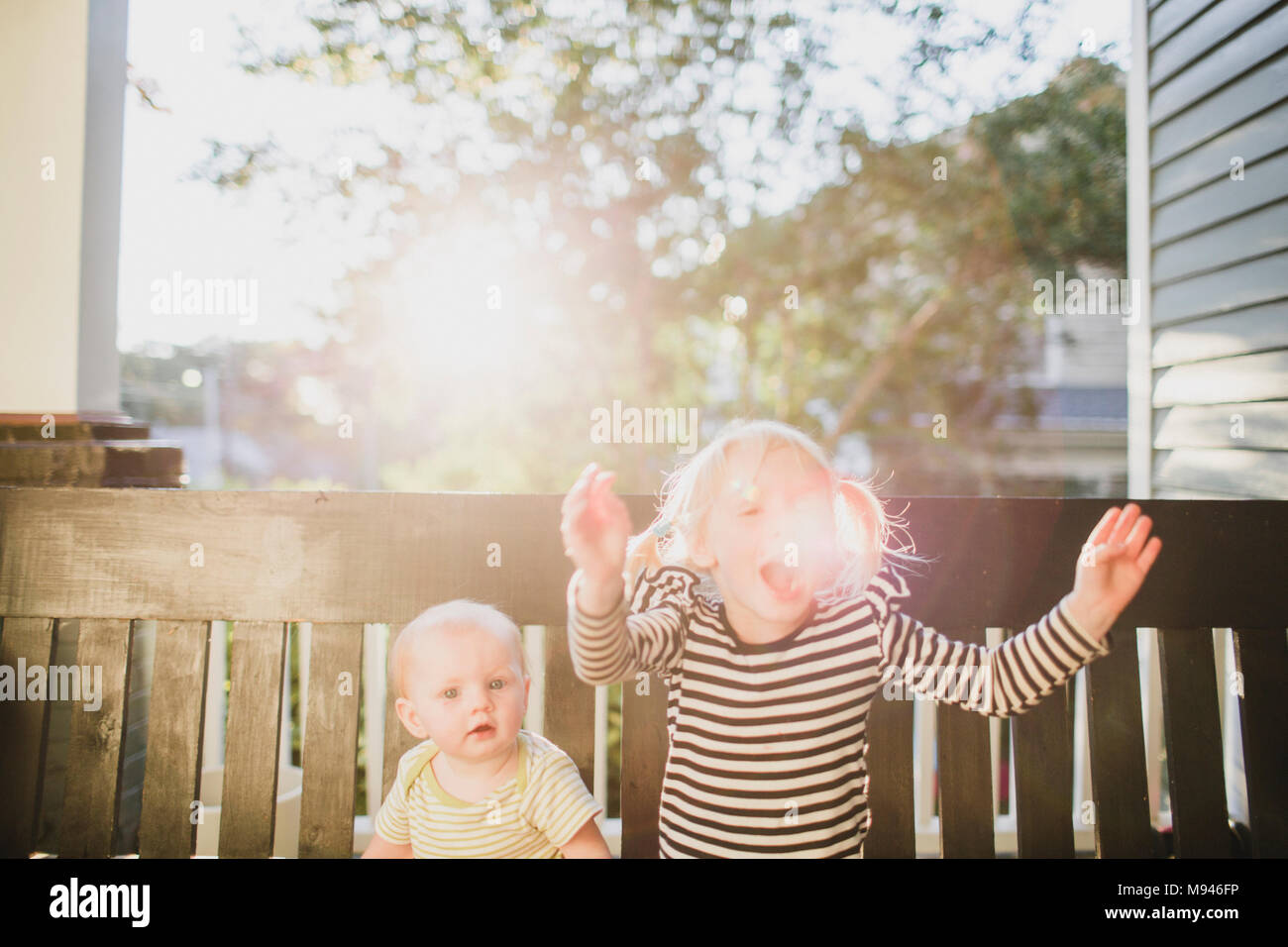 Ragazza e baby sitting su banco nella luce del sole Foto Stock