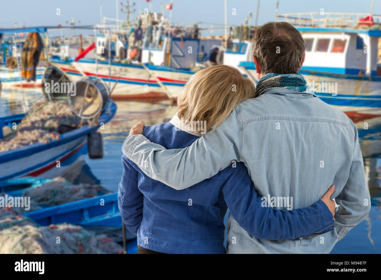 Midle invecchiato amare giovane in piedi e ammirando lungo il fronte mare con barche da pesca nella baia in Tunisia Foto Stock
