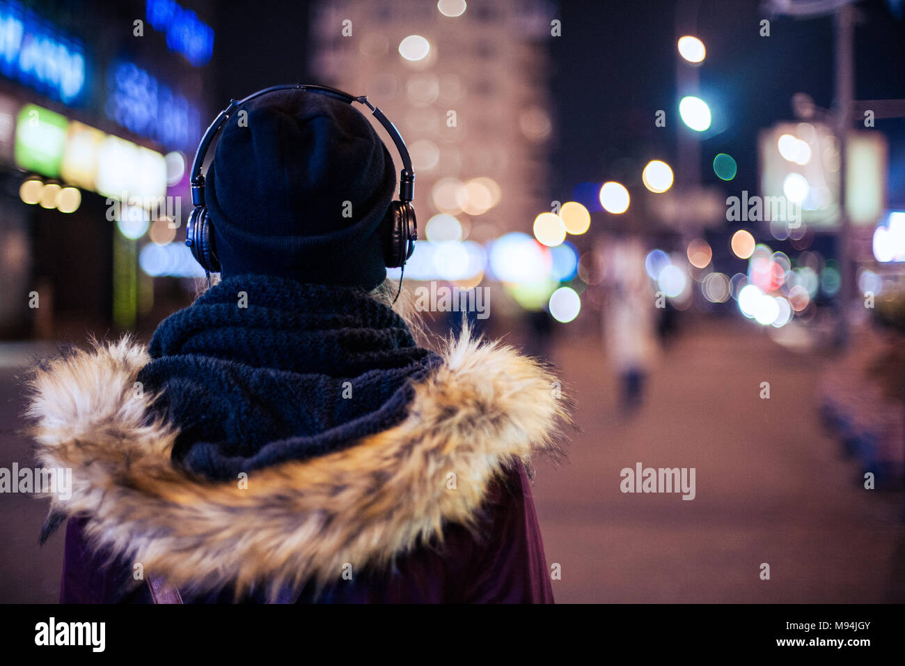 Vista posteriore di un hipster ragazza camminare attraverso la città di notte street l'ascolto della musica Foto Stock