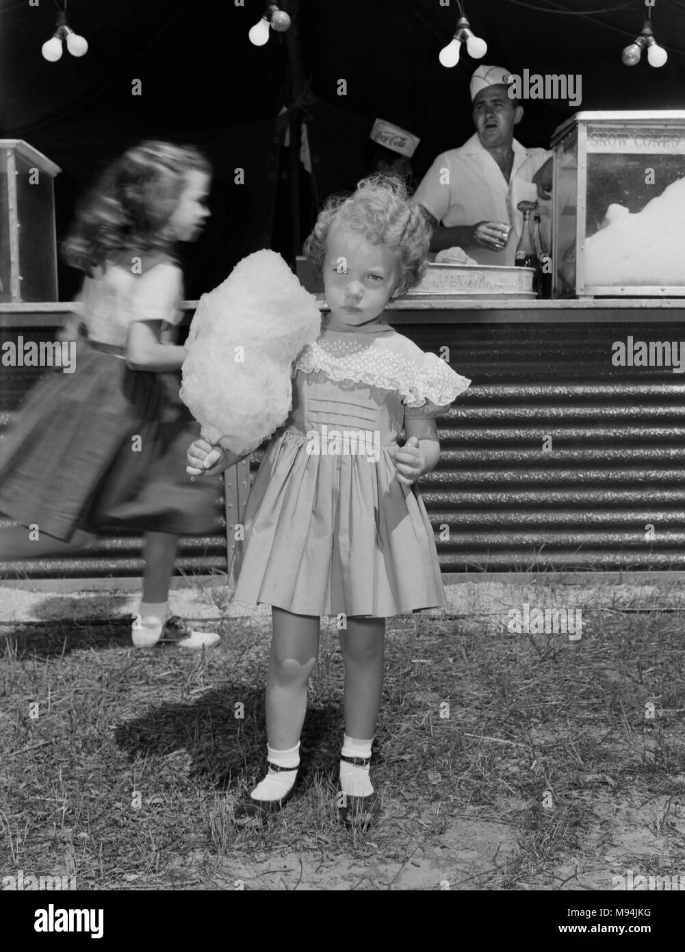 Un grave bambina mantiene la sua caramella di cotone mentre in un circo in Georgia rurale, ca. 1960. Foto Stock