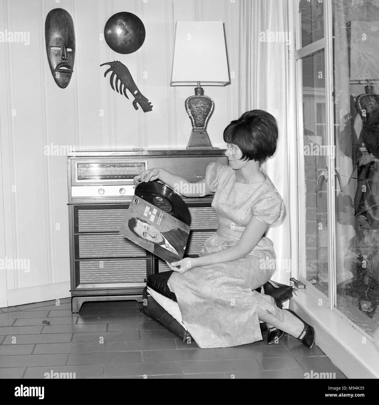Giovane donna riproduce una registrazione LP sul suo nuovo impianto stereo hi-fi entertainment center in California, ca. 1964. Foto Stock