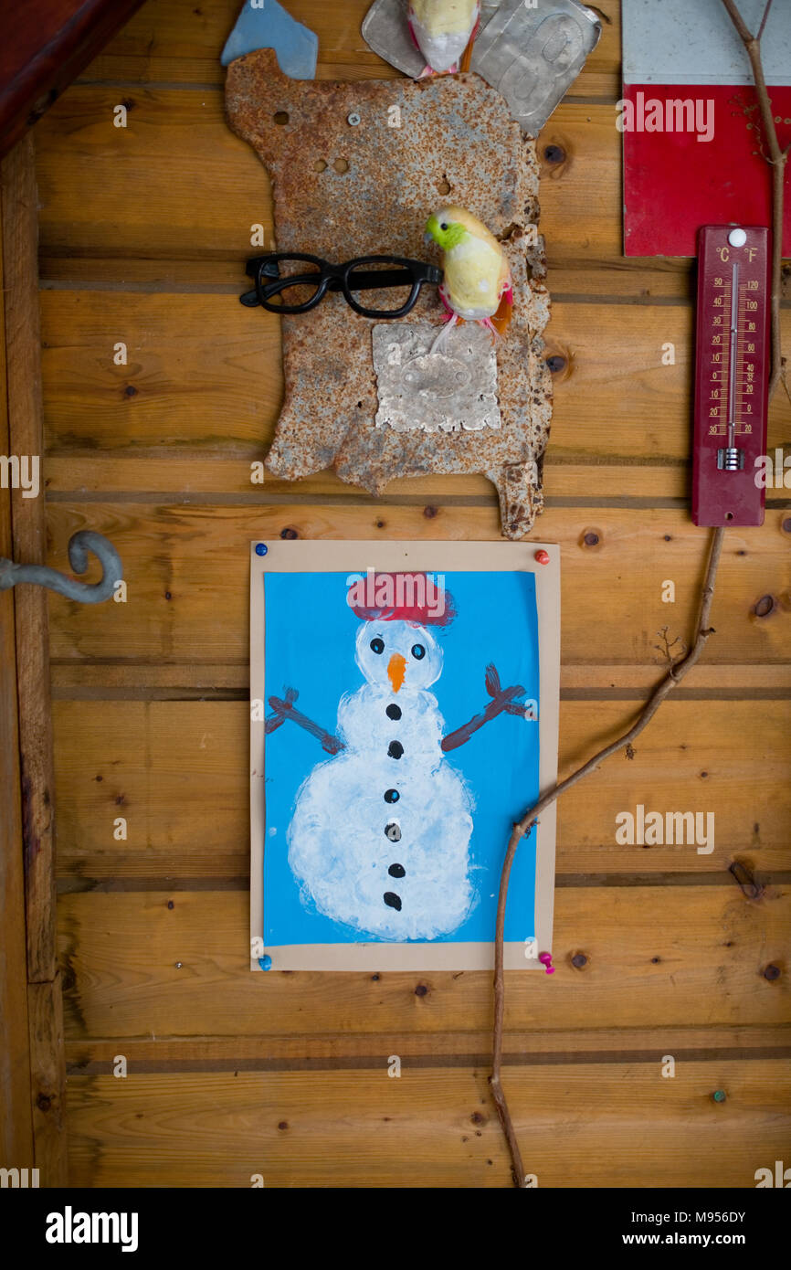 Un bambino del dipinto di un pupazzo di neve è imperniata ad una parete in legno di uno chalet accanto a una serie di altri oggetti trovati, compreso un termometro Foto Stock