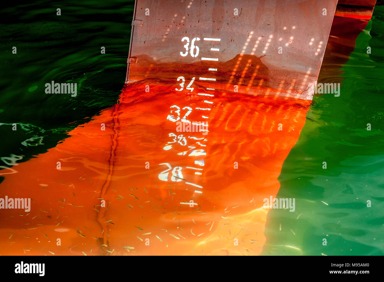 La poppa della nave con timone di rosso e bianco e il numero di incrementi in acque poco profonde che mostra la distorsione di rifrazione come i pesci nuotano intorno ad esso Foto Stock