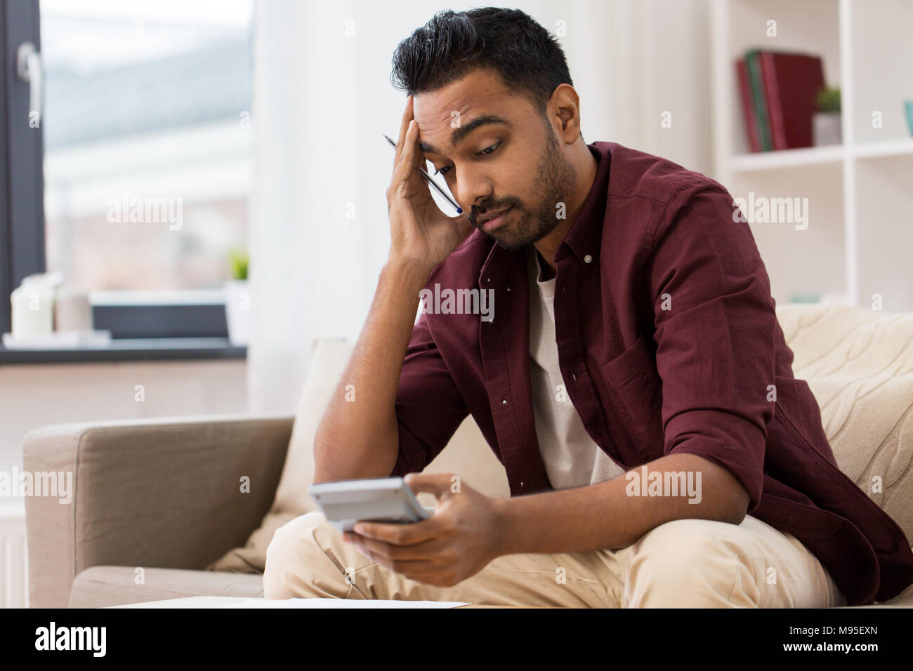Uomo confuso con la calcolatrice a casa Foto Stock