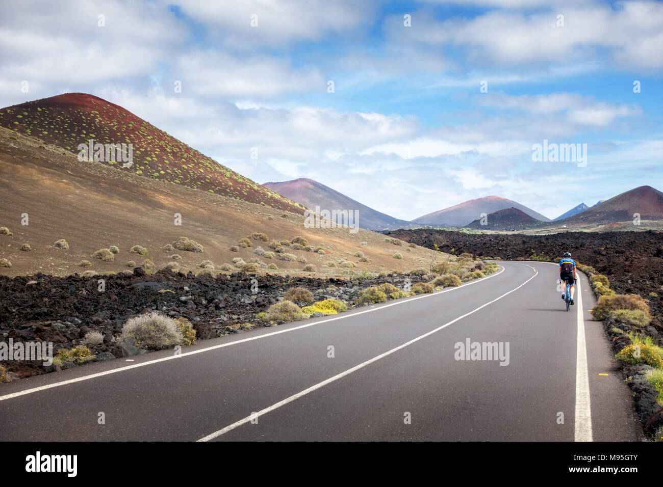 Persona in sella ad una bicicletta pedalando su una strada vuota attraverso la El Golfo Parco Nazionale in Lanzarote Foto Stock