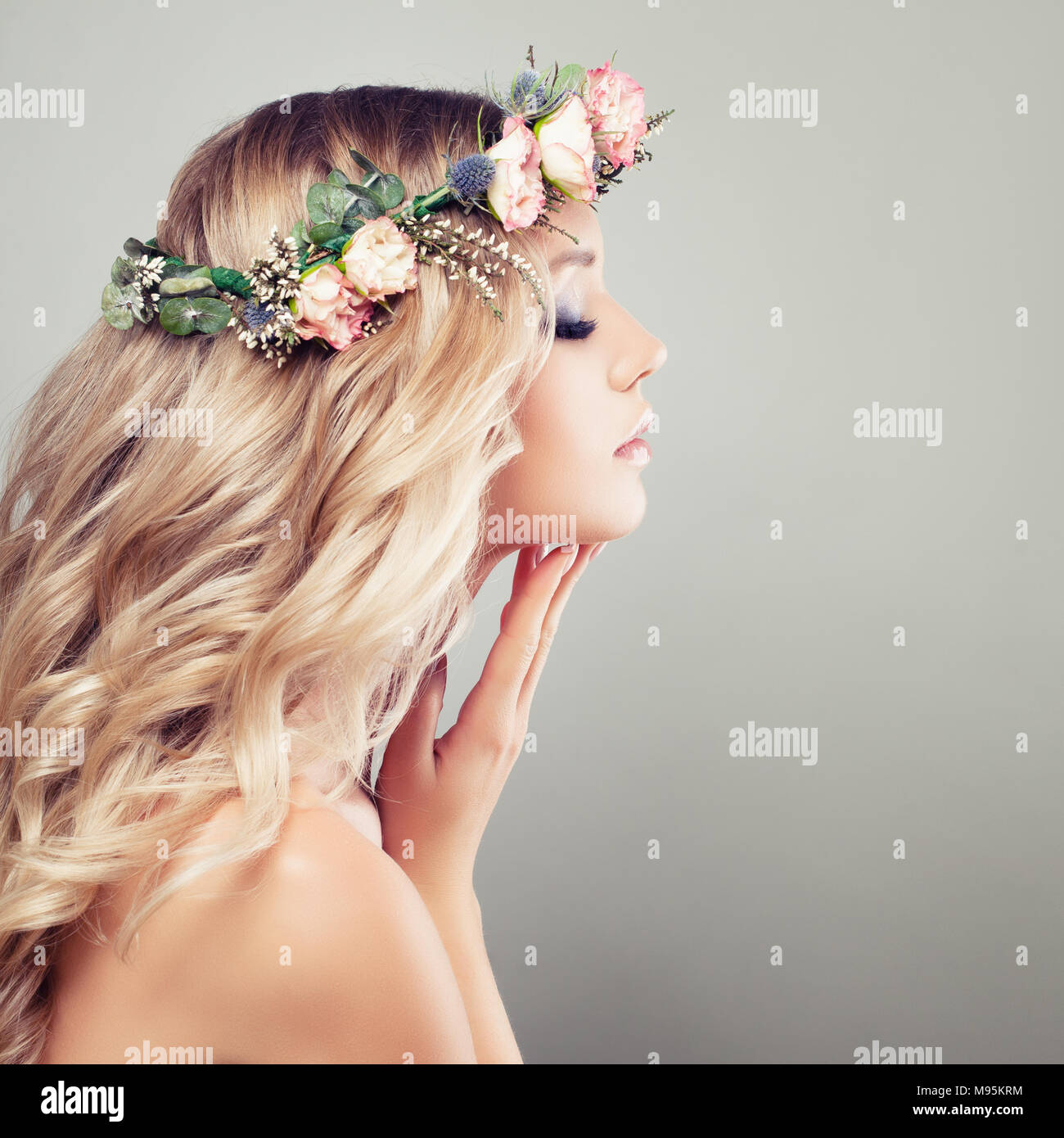 Giovane Bella Donna con fiori nei capelli. Modello di sani con il trucco e biondo Curly acconciatura sul background, Spa Beauty e cosmetologia nozione Foto Stock