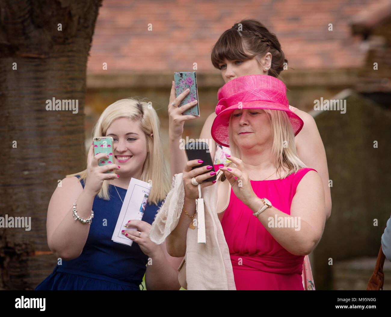 Gli ospiti femminili ad un matrimonio prendendo fotografie su telefoni cellulari Foto Stock