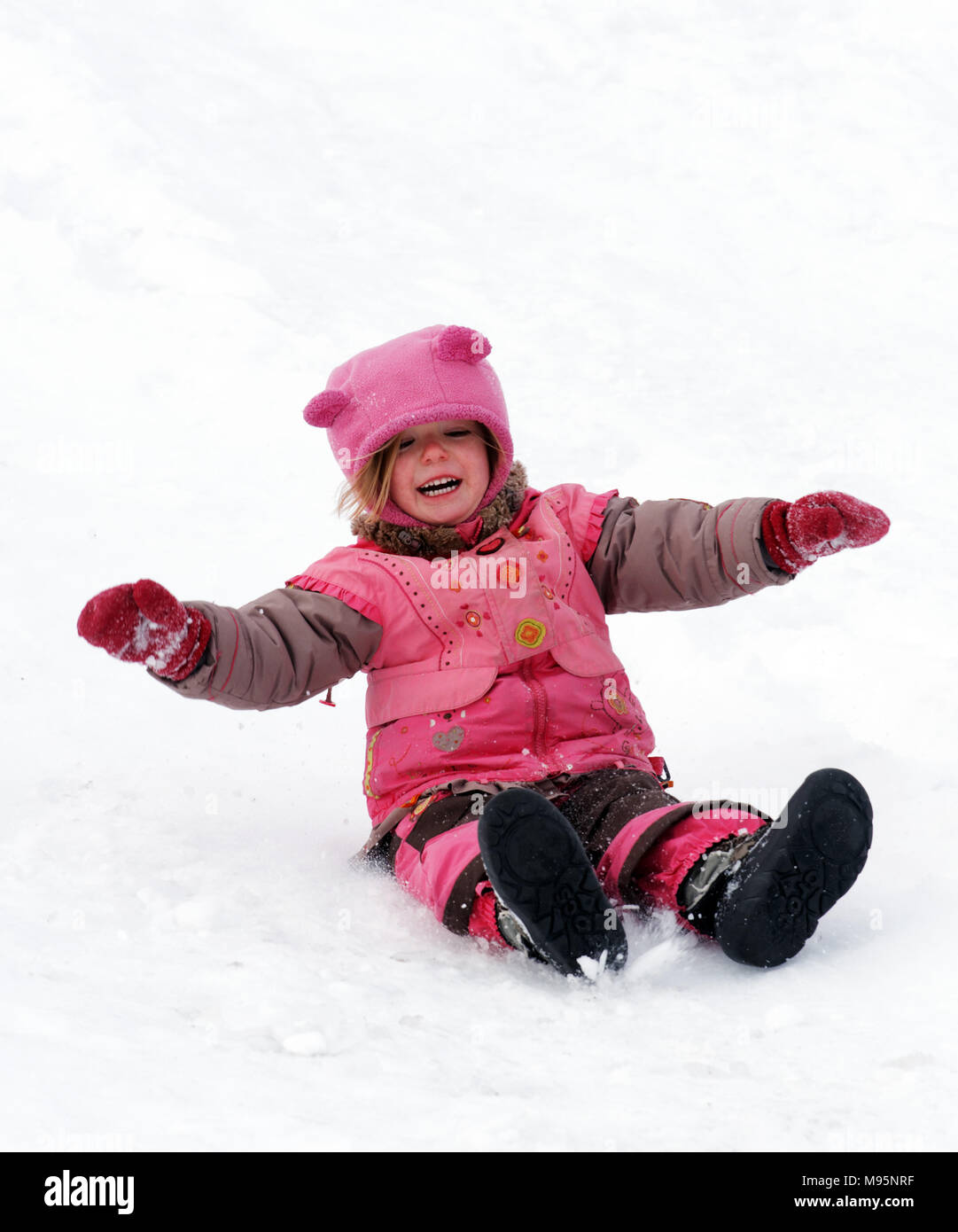 Un ridere bambina di tre anni scorrevole su il culo nella neve in Québec Canada Foto Stock