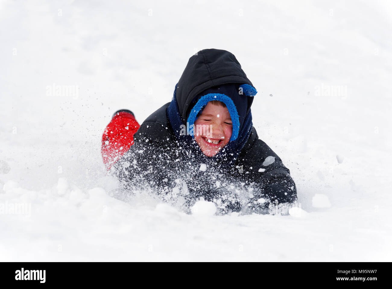 Un piccolo ragazzo (5 yr old) smorfie come la neve entra nel suo volto come egli faccia diapositive prima nella neve Foto Stock