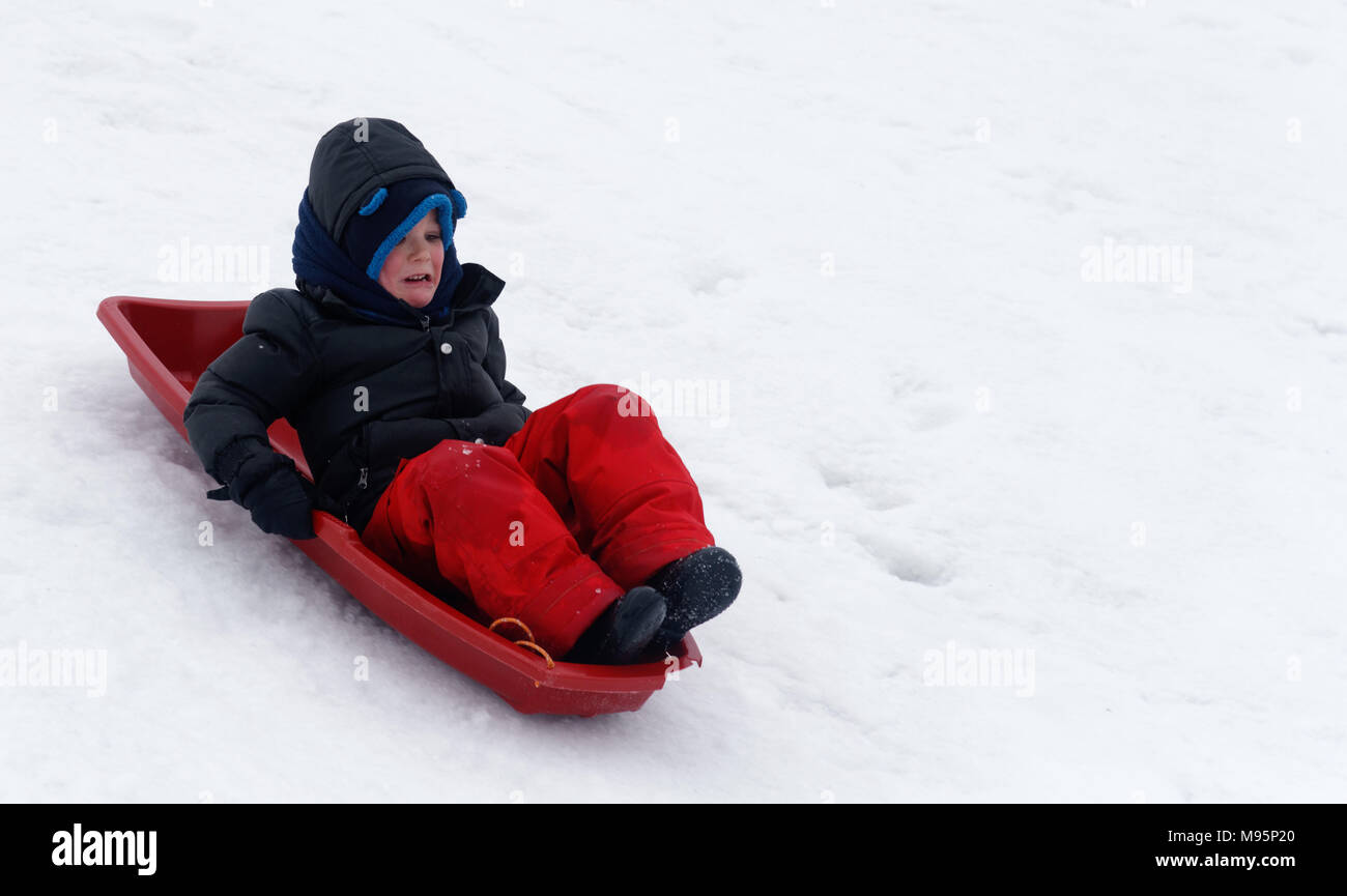 Un piccolo ragazzo (5 yr old) cercando paura come egli slitte verso il basso un ripido pendio ghiacciato Foto Stock