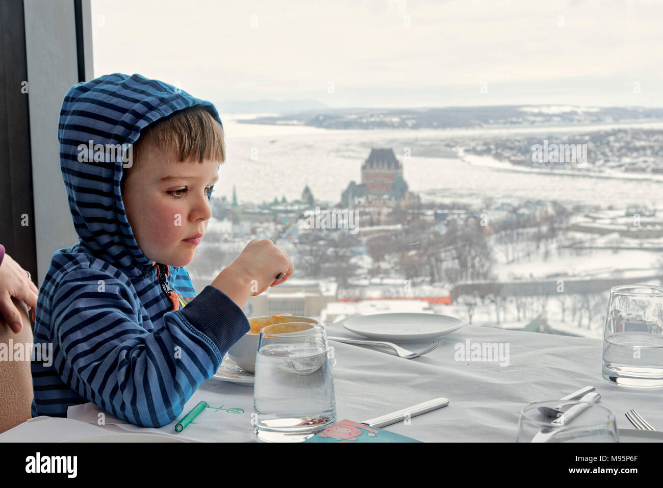 Un bambino di cinque anni, ragazzo di mangiare in Ciel! Il ristorante rotante in Quebec City, con lo Chateau Frontenac e congelata di St Lawrence al di là. Foto Stock