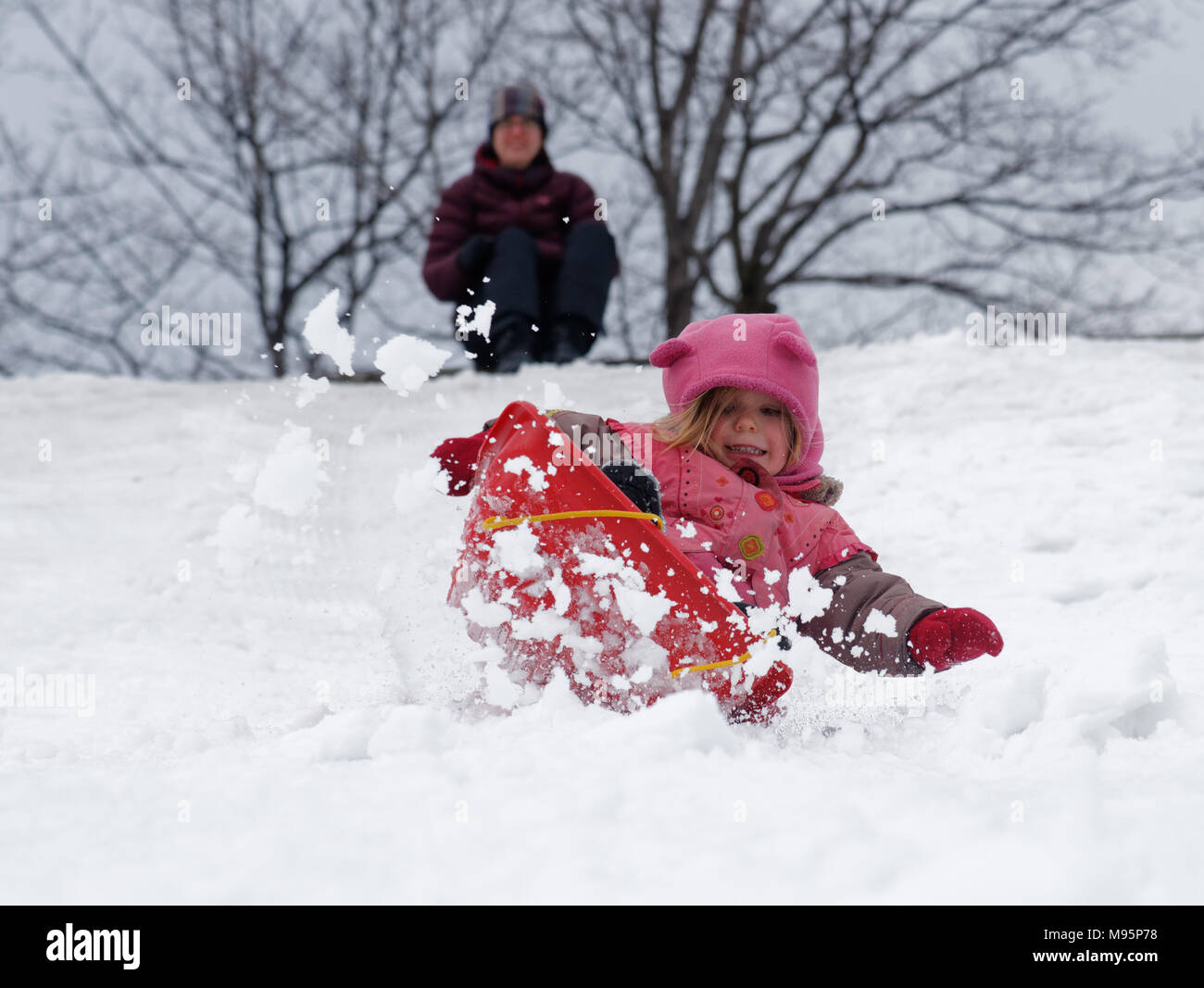 Una bambina di 3 anni) in slittino Québec Canada con mamma al di là, guardando a. Foto Stock