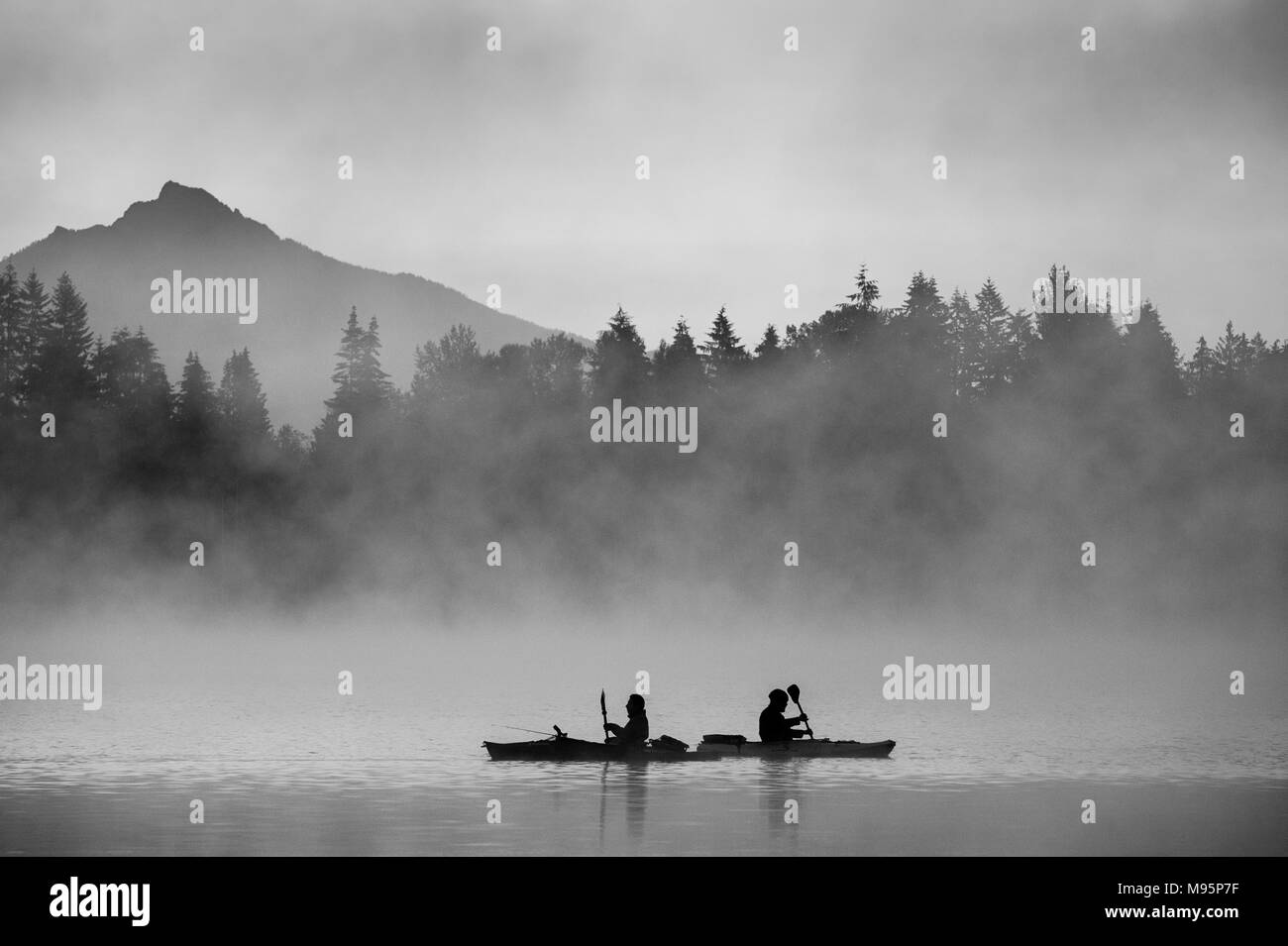 I pescatori in kayak alba sul lago Cassidy con la nebbia e la Cascade Mountain Range su alberi. Foto Stock