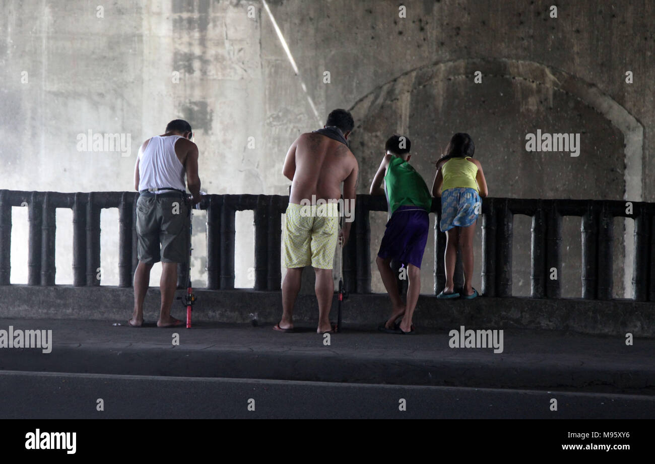 4 persone vista fom la schiena stanno pescando su a. fiume in una strada di Manila nelle filippine Foto Stock