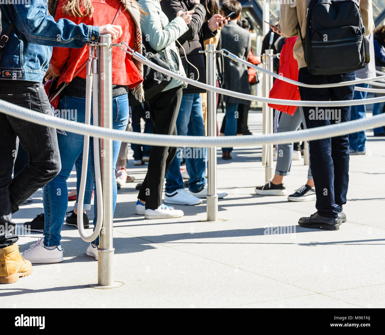 Le persone in piedi in linea tra acciaio inossidabile coda poli grigio con funi, all'ingresso di un sito turistico, poggiando sui pali o guardare i loro Foto Stock