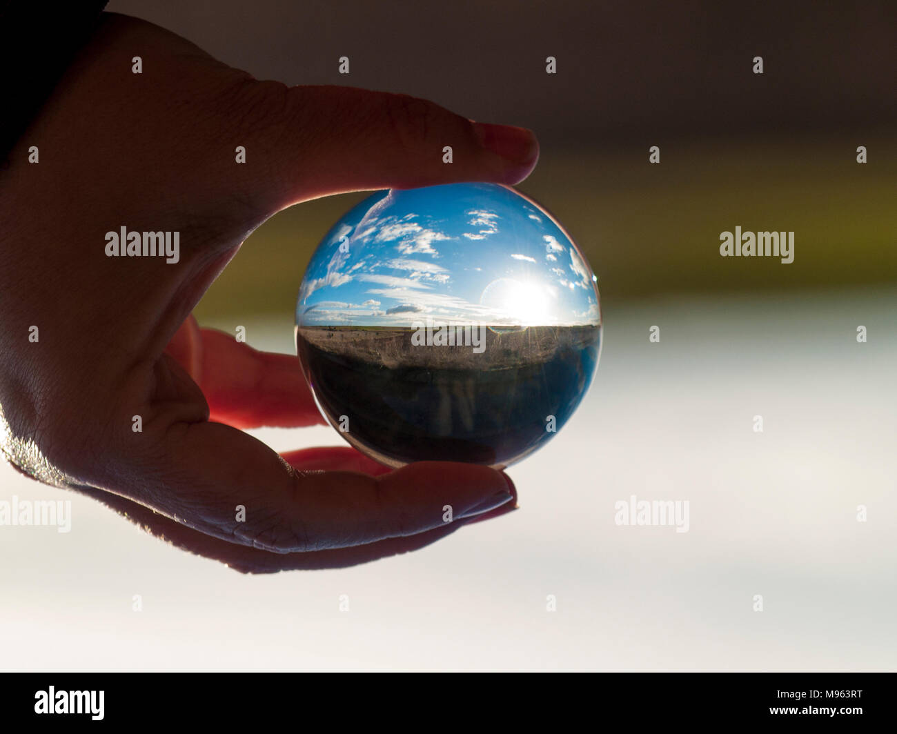 Donna mano azienda sfera di vetro con vista panoramica della campagna e cielo blu/ concetto per l ambiente Foto Stock