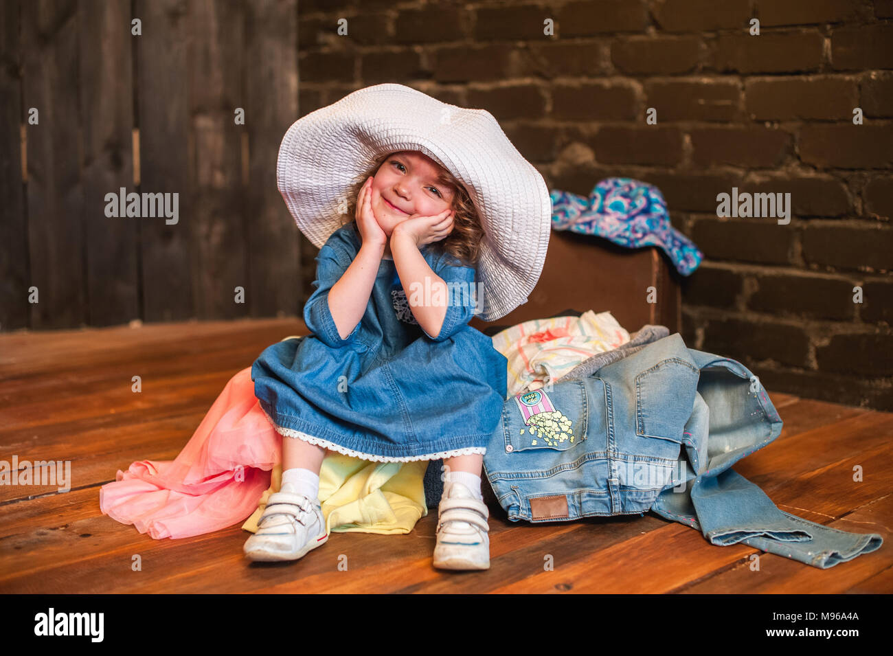 Bambina con cappello bianco seduta in valigia con le cose e guardare la  fotocamera. Viaggiare con i bambini Foto stock - Alamy