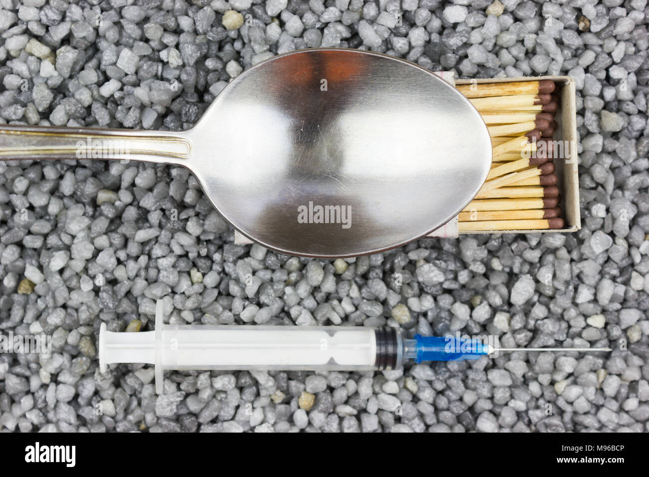 Siringa plastica, un cucchiaio e una corrispondenza sulla ghiaia fine. Medicina, Medicina. Il consumo di droghe. Foto Stock