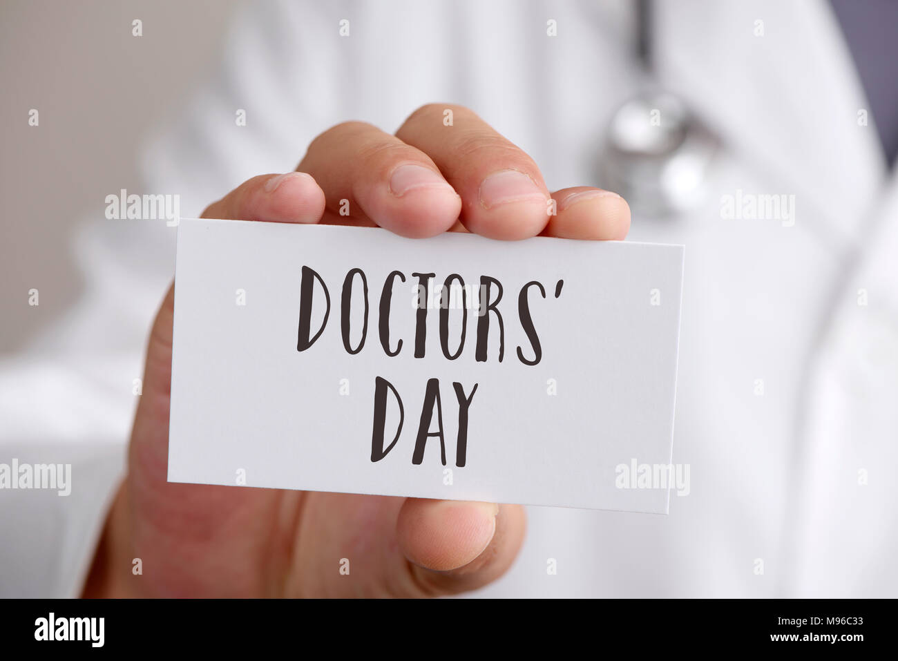 Primo piano di un giovane medico caucasica uomo, indossando il camice bianco, mostrando un cartello con scritto il testo medici giorno scritto in esso Foto Stock