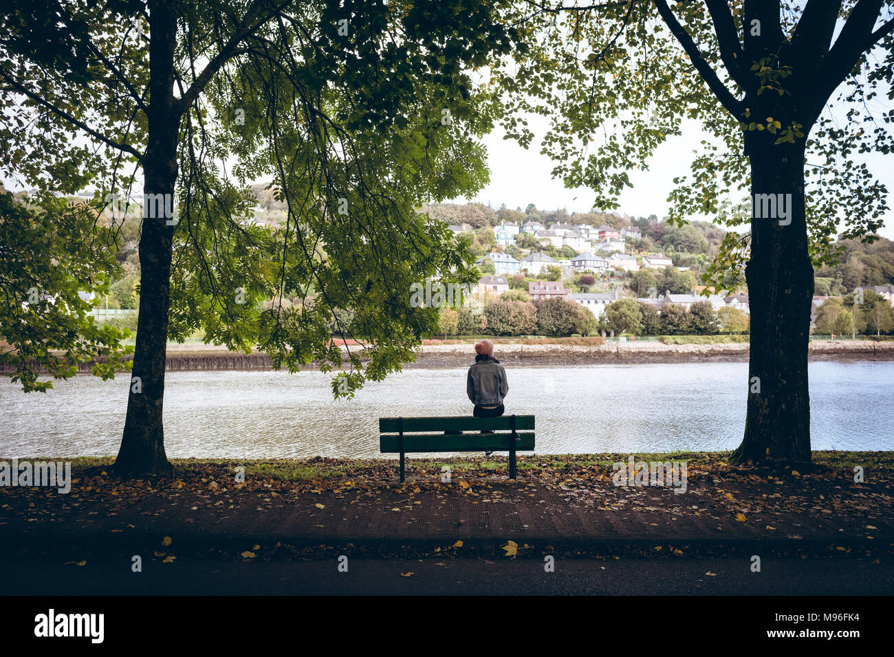 Giovane donna seduta sul banco vicino al fiume costa a park Foto Stock