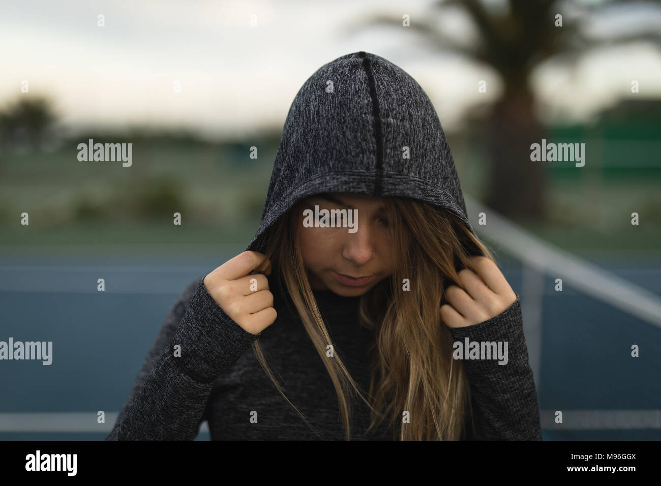 Donna in piedi in felpa con cappuccio a campo da tennis Foto Stock