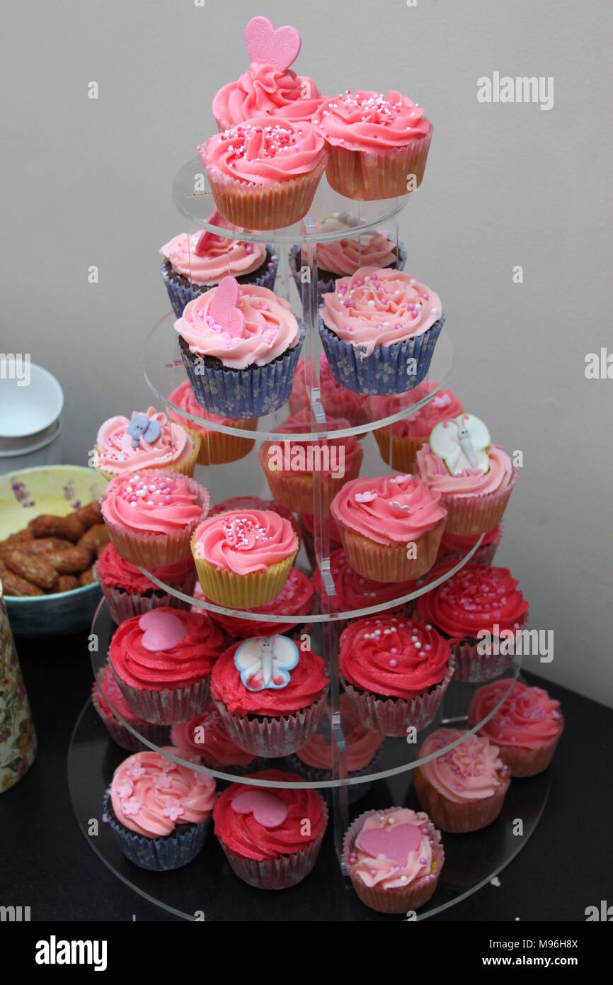 Cinque tier cake stand riempito con tortine coperti in diverse sfumature di rosa glassa e decorazioni di cuore solo una tabella con una ciotola di salsicce chipolata Foto Stock