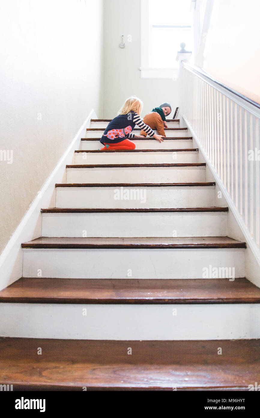 Ragazza aiutando baby strisciare su per le scale Foto Stock