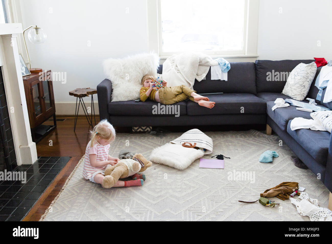 Ragazza posa sul divano con il bambino che gioca con orso sul pavimento Foto Stock