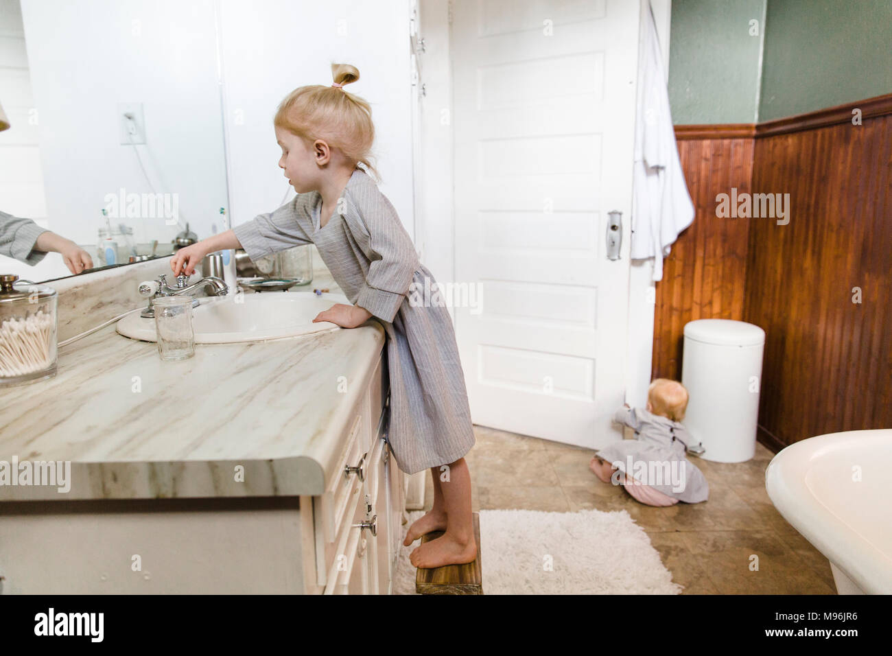 Ragazza con lavandino mentre il bambino si siede sul pavimento del bagno Foto Stock