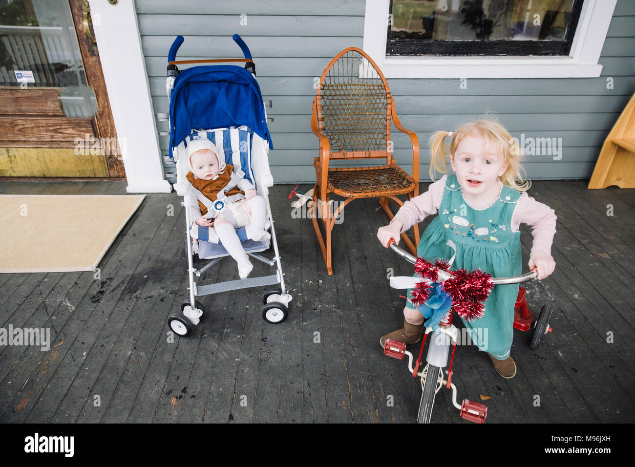 Ragazza con il triciclo accanto al bambino in blu la PRAM/passeggino Foto Stock